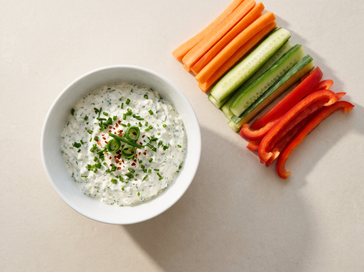 Kräuter-Hüttenkäse-Dip in einer weissen Schale mit Gemüsesticks