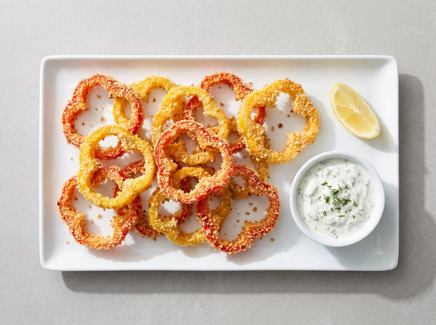 Knusprige panierte Paprikaringe mit Joghurt-Dip auf einer weissen Platte
